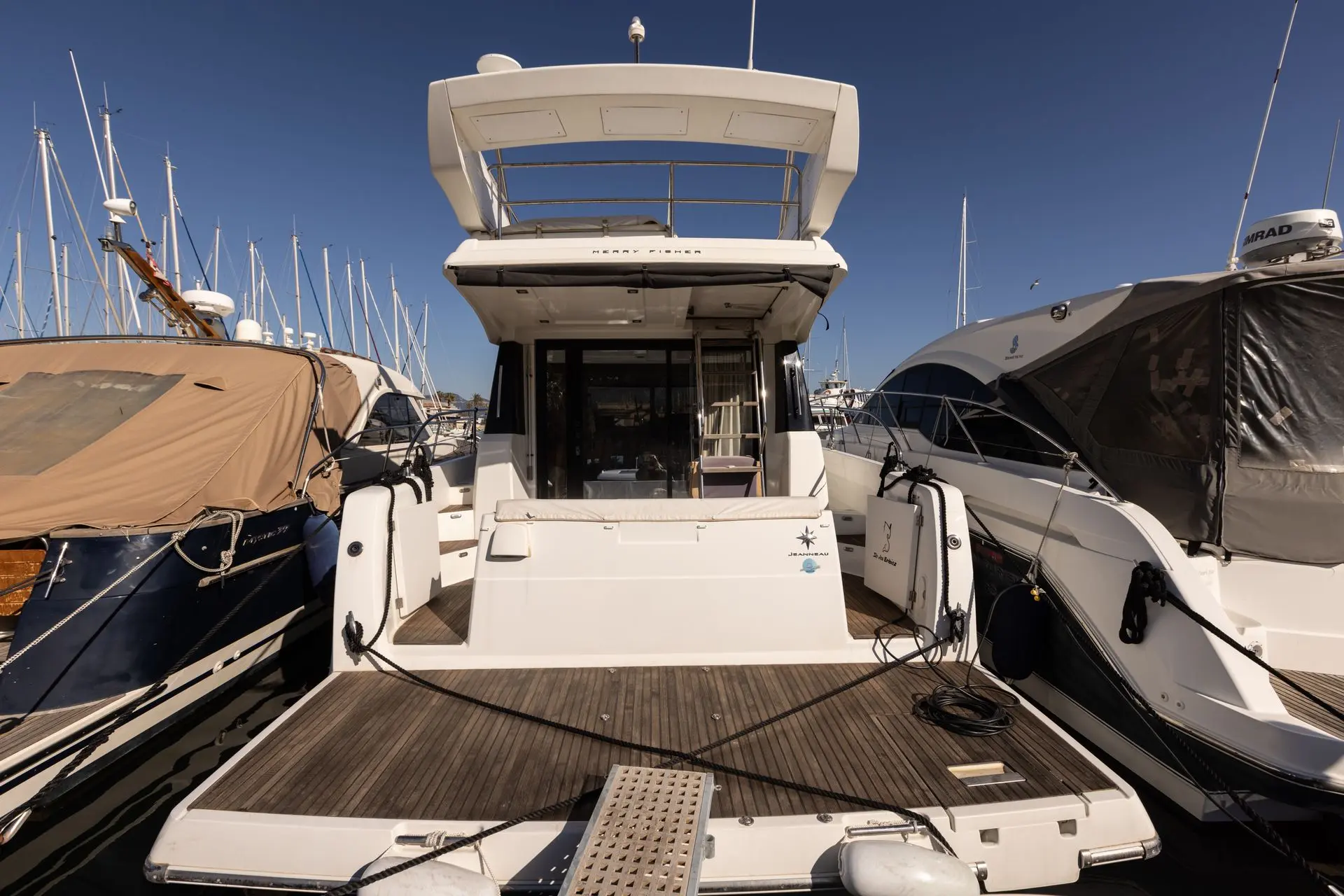 Jeanneau Merry Fisher 38 Fly — Vue arrière d’un bateau à moteur amarré dans un port, entre deux autres bateaux.