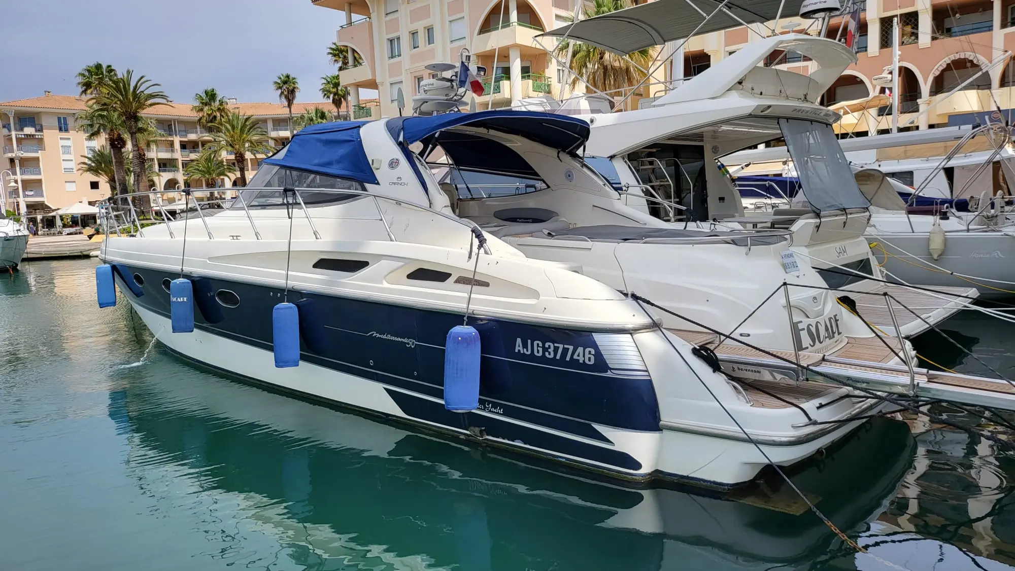 Cranchi Mediterranee 50 — Bateau à moteur blanc et bleu amarré dans une marina, vu de trois quarts arrière.