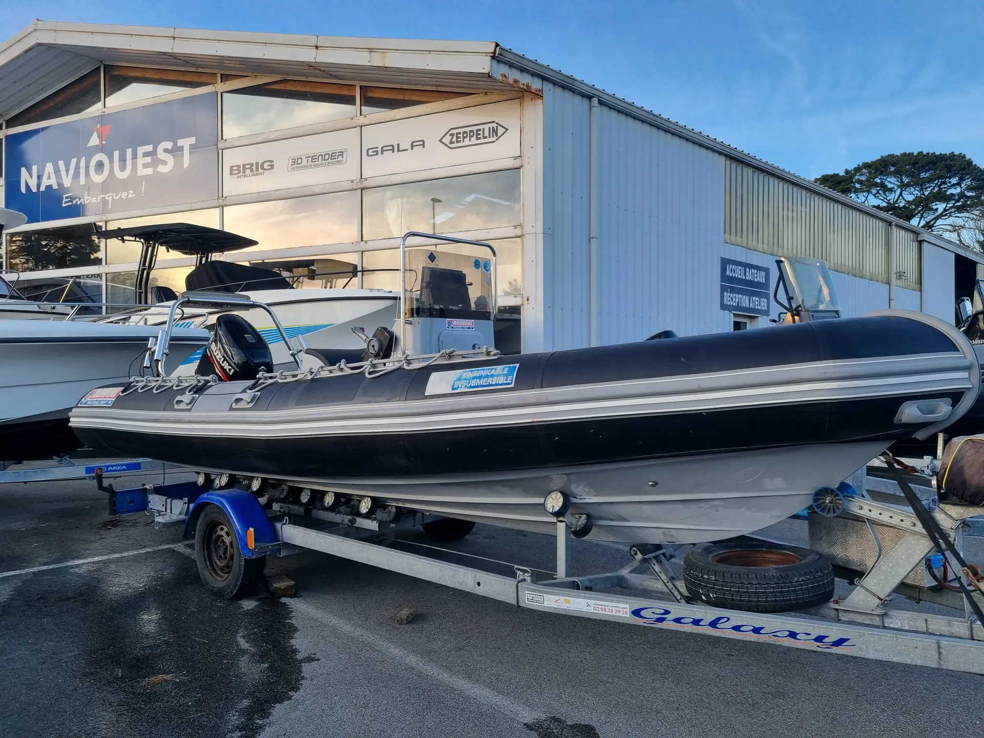 Narwhal WB 620 — Bateau semi-rigide noir exposé sur sa remorque devant un bâtiment nautique.