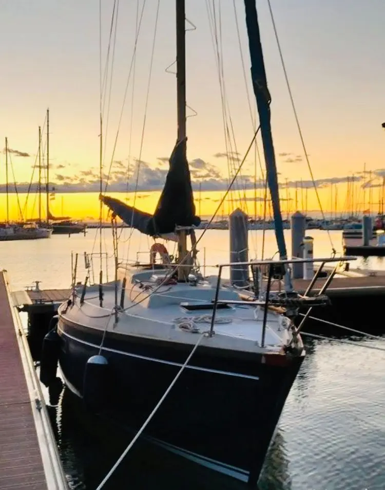 Dufour 27 — Voilier amarré dans un port au coucher du soleil, vu de trois quarts avant.