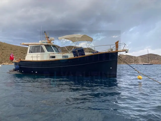 Menorquin 120 — Bateau à moteur bleu et blanc au mouillage dans une baie montagneuse.