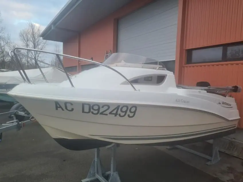 Quicksilver Activ 430 Cabin — Bateau à moteur blanc sur remorque, photographié de profil devant un bâtiment.
