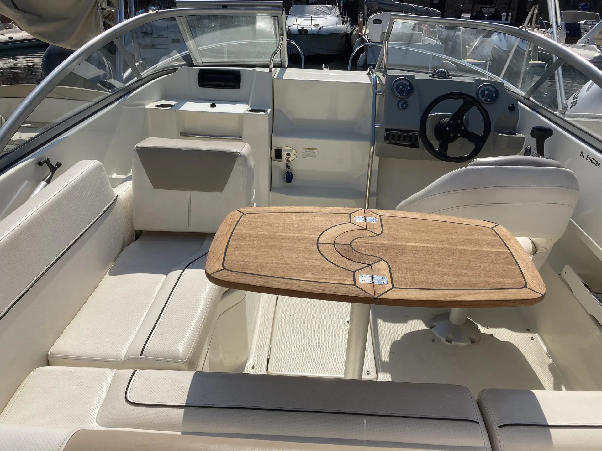 Bayliner 642 CU — Vue du cockpit avec banquettes, table, pare-brise et poste de pilotage.