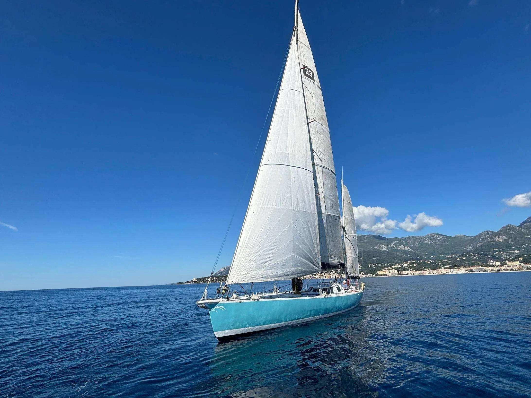 Garcia Eclipse 60 — Voilier bleu naviguant au large, toutes voiles hissées, devant une côte montagneuse.