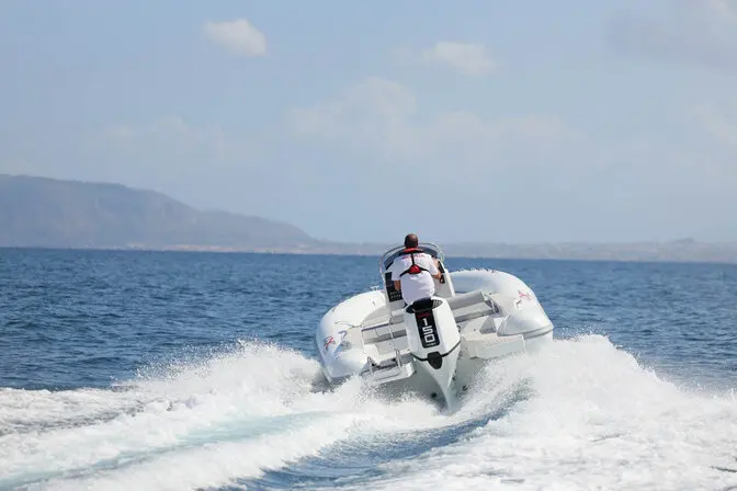 4XC HA23 — Un bateau pneumatique file au large, vu de l’arrière, avec une personne à bord.