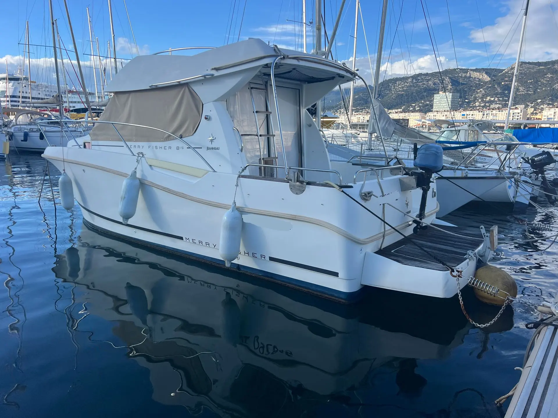 Jeanneau Merry Fisher 815 — Bateau à moteur blanc amarré, vu de trois quarts arrière dans un port.