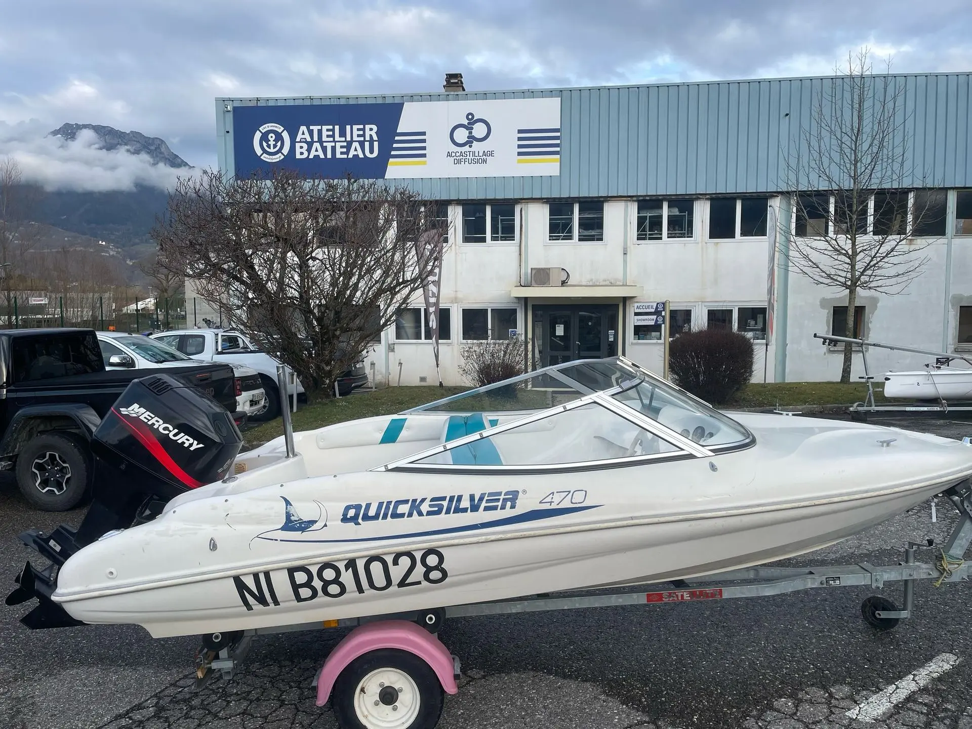 Quicksilver 470 Sport — Bateau à moteur blanc présenté sur remorque devant un atelier nautique.