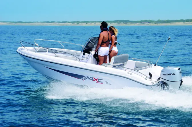 4XC H19CC — Bateau à moteur blanc naviguant près d’une côte, avec deux personnes à bord.