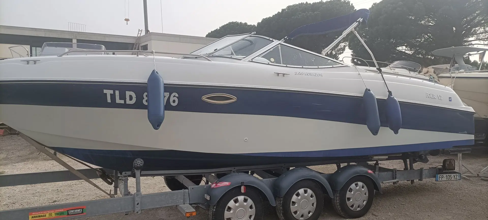 Four Winns Horizon 240 — Bateau à moteur bleu et blanc présenté sur une remorque, vu de profil.