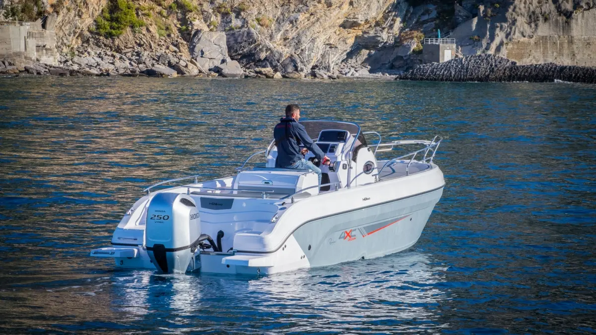4XC H26SD — Bateau à moteur blanc vu de trois-quarts arrière, avec une personne à la barre.