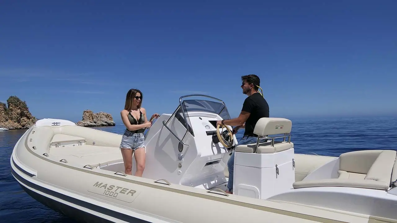 Master 1000 — Bateau semi-rigide blanc avec deux personnes à bord, au large d'une côte rocheuse.