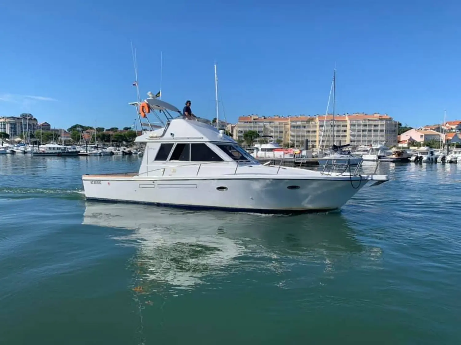 Guy Bonnet 41 — Bateau à moteur blanc vu de profil dans un port, avec une personne sur le toit.