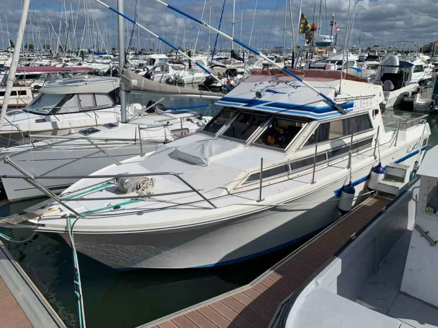 Jeanneau Almeria 960 — Bateau à moteur blanc et bleu amarré dans un port de plaisance.