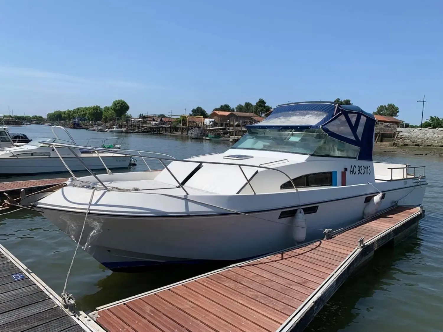 Guy Couach Pyla 1000 — Bateau à moteur blanc amarré à un ponton, vu de trois quarts avant.