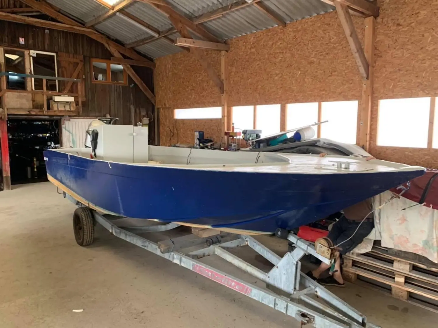Trident Marine Plate — Bateau bleu et blanc posé sur une remorque dans un hangar.