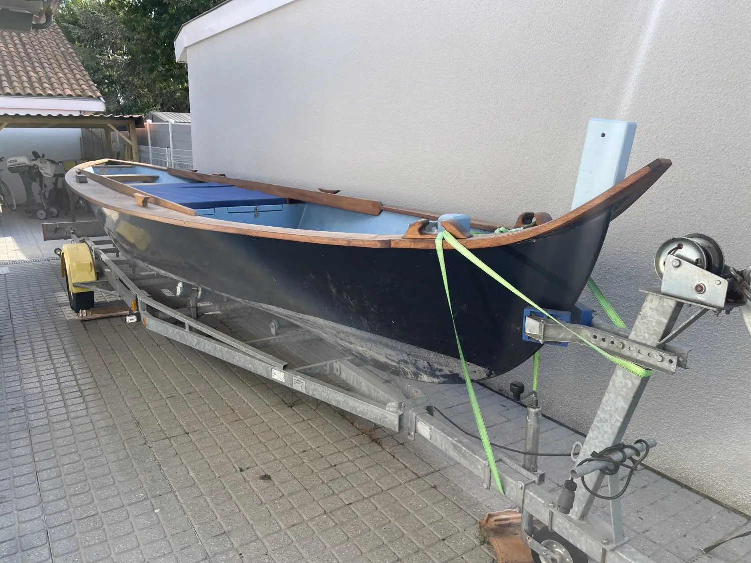 Windrider Pinassotte — Bateau à coque sombre et bordés en bois présenté sur une remorque.