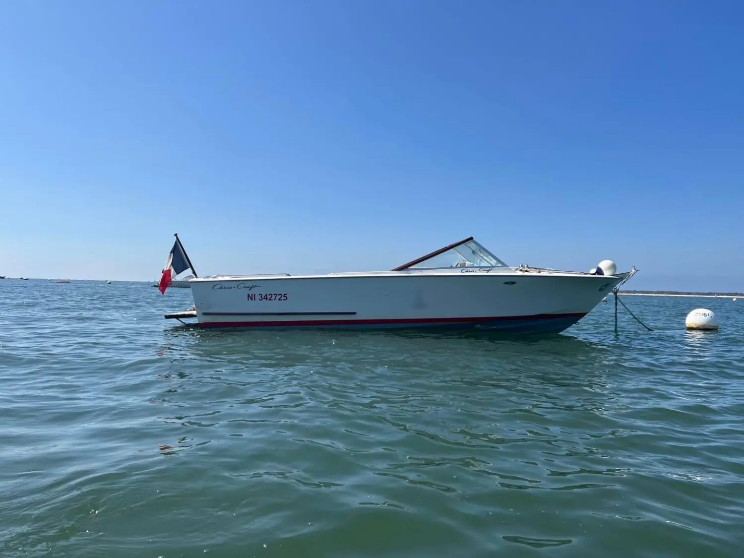 Chris Craft Lancer 23 — Bateau blanc vu de profil, amarré sur une étendue d’eau par temps dégagé.