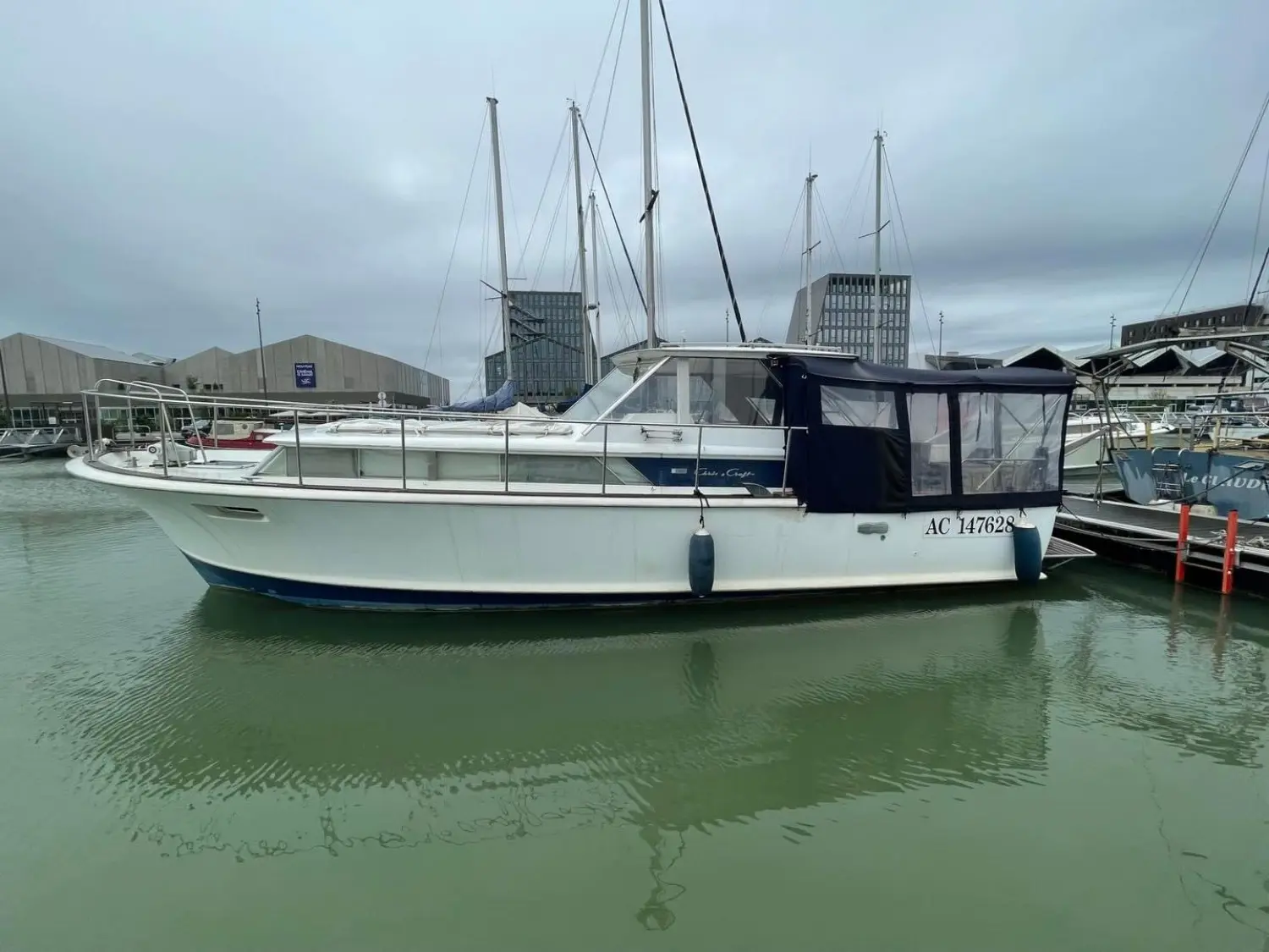 Chris Craft Commander 38 — Bateau à moteur blanc amarré dans une marina, vu de profil par temps couvert.