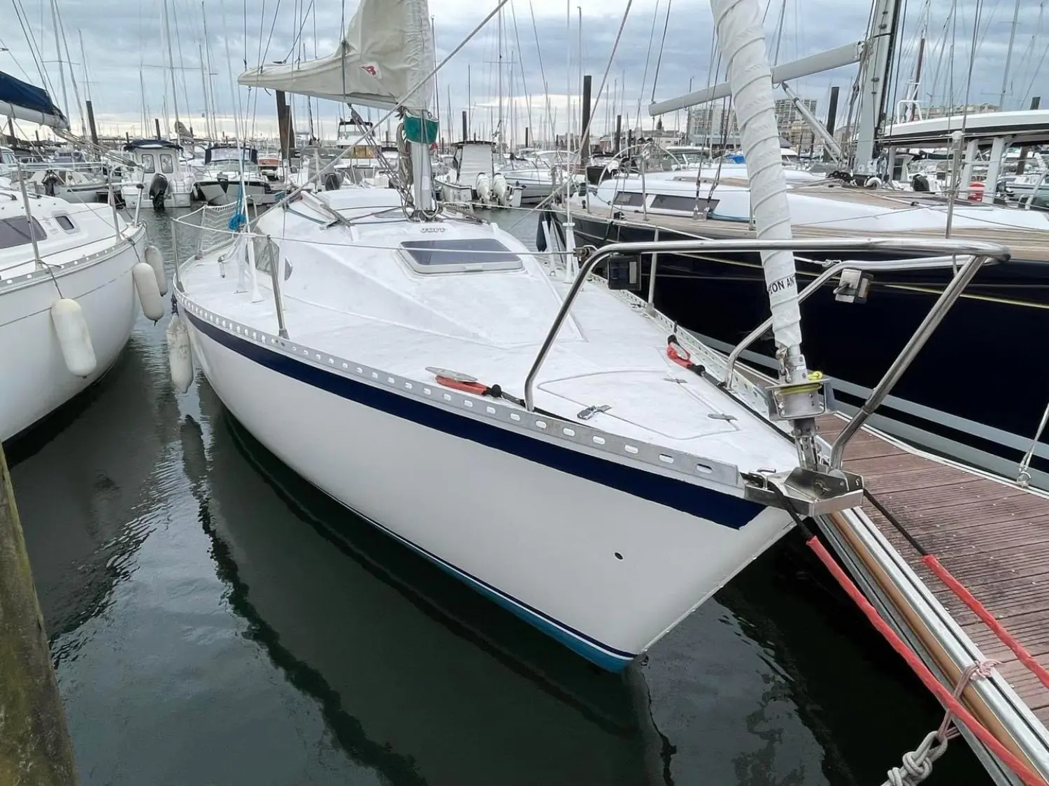 Gibert Marine Gib Sea 77 — Voilier blanc à bande bleue amarré dans un port, vu de trois quarts avant.