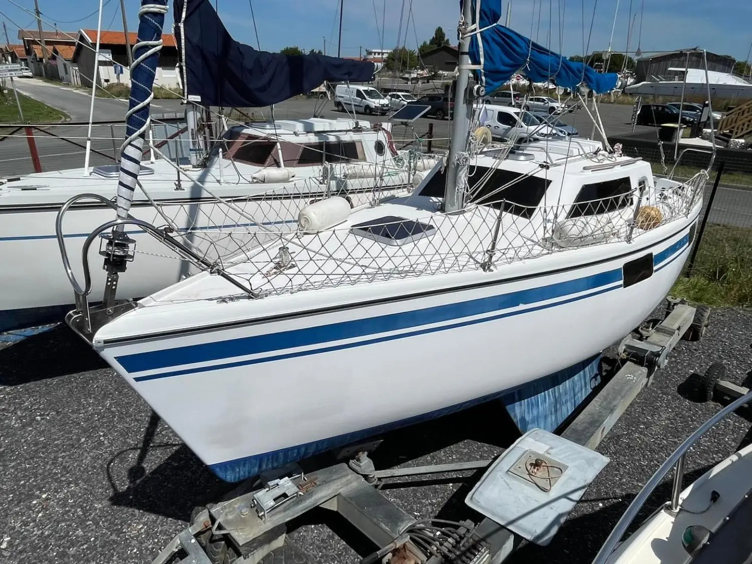 Wrighton Biloup 77 Nv — Voilier blanc à bandes bleues, photographié à terre sur sa remorque.
