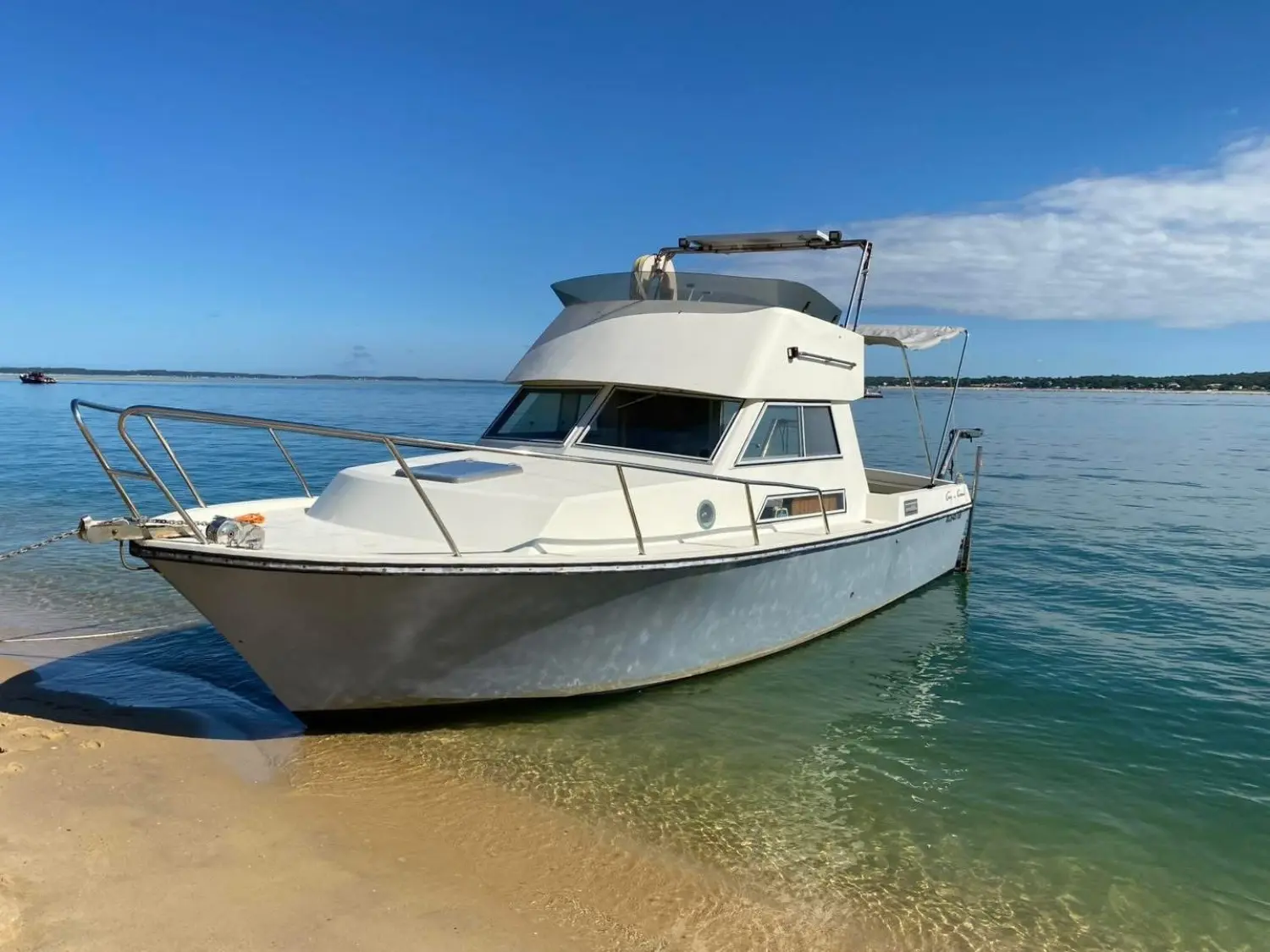 Guy Couach 730 — Vedette à cabine blanche photographiée près d’une plage, sur une eau calme.