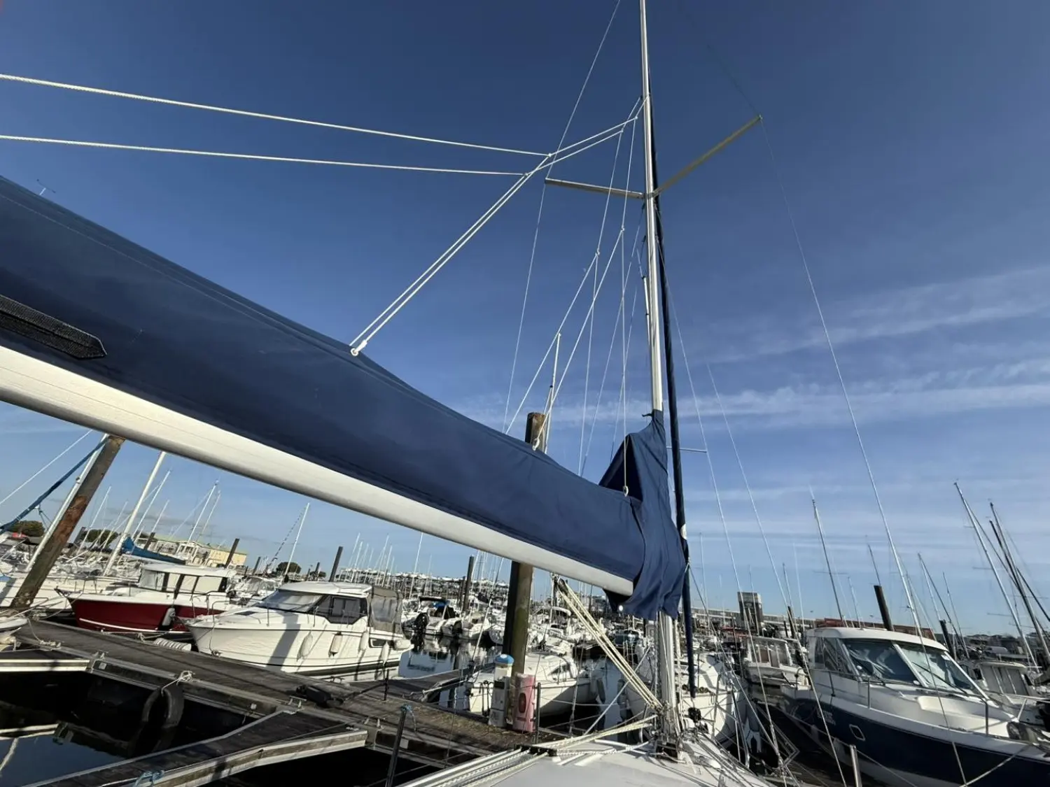 Maxus 24 — Vue partielle d'un voilier amarré dans un port, avec le mât et la bôme au premier plan.