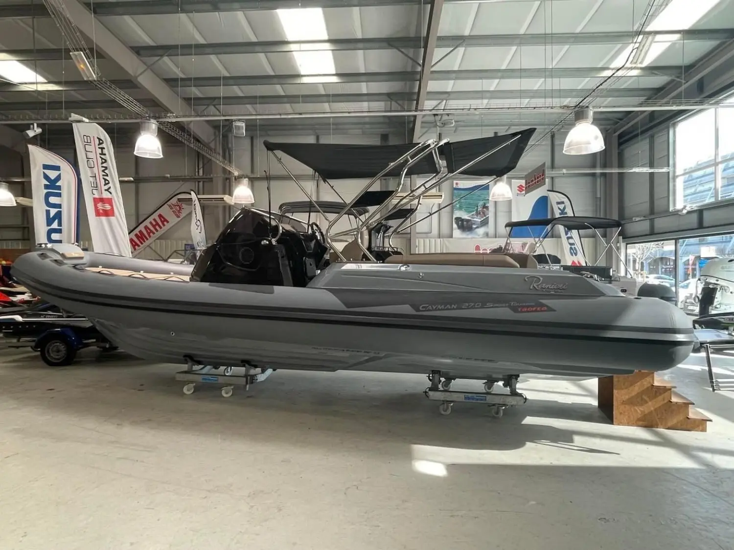 Ranieri Cayman 27 Sport Touring Trofeo — Bateau semi-rigide gris présenté de profil sur remorque dans un showroom.