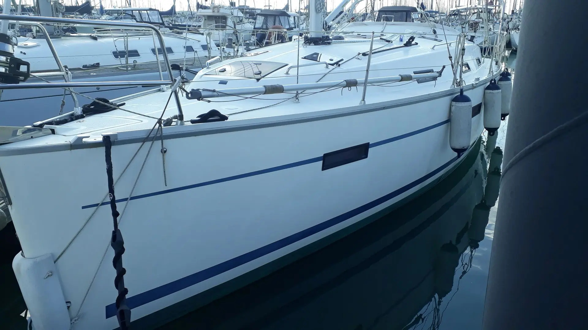 Bavaria Cruiser 36 — Voilier blanc amarré vu de trois quarts dans un port, entouré d'autres bateaux.