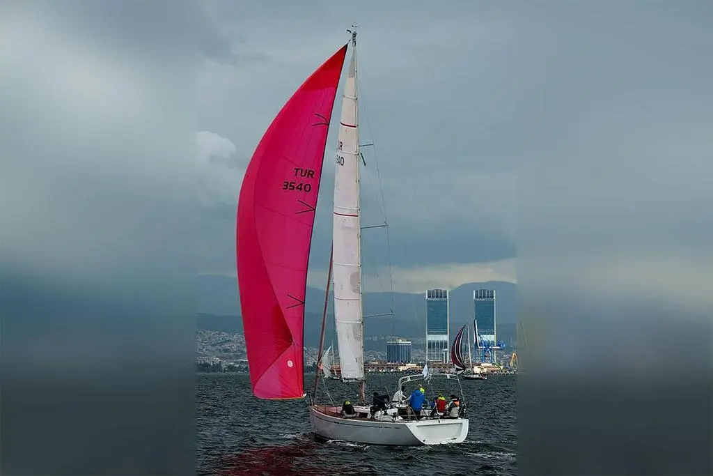 Grand Soleil 40 — Voilier de course sous spi rose devant une ville côtière.