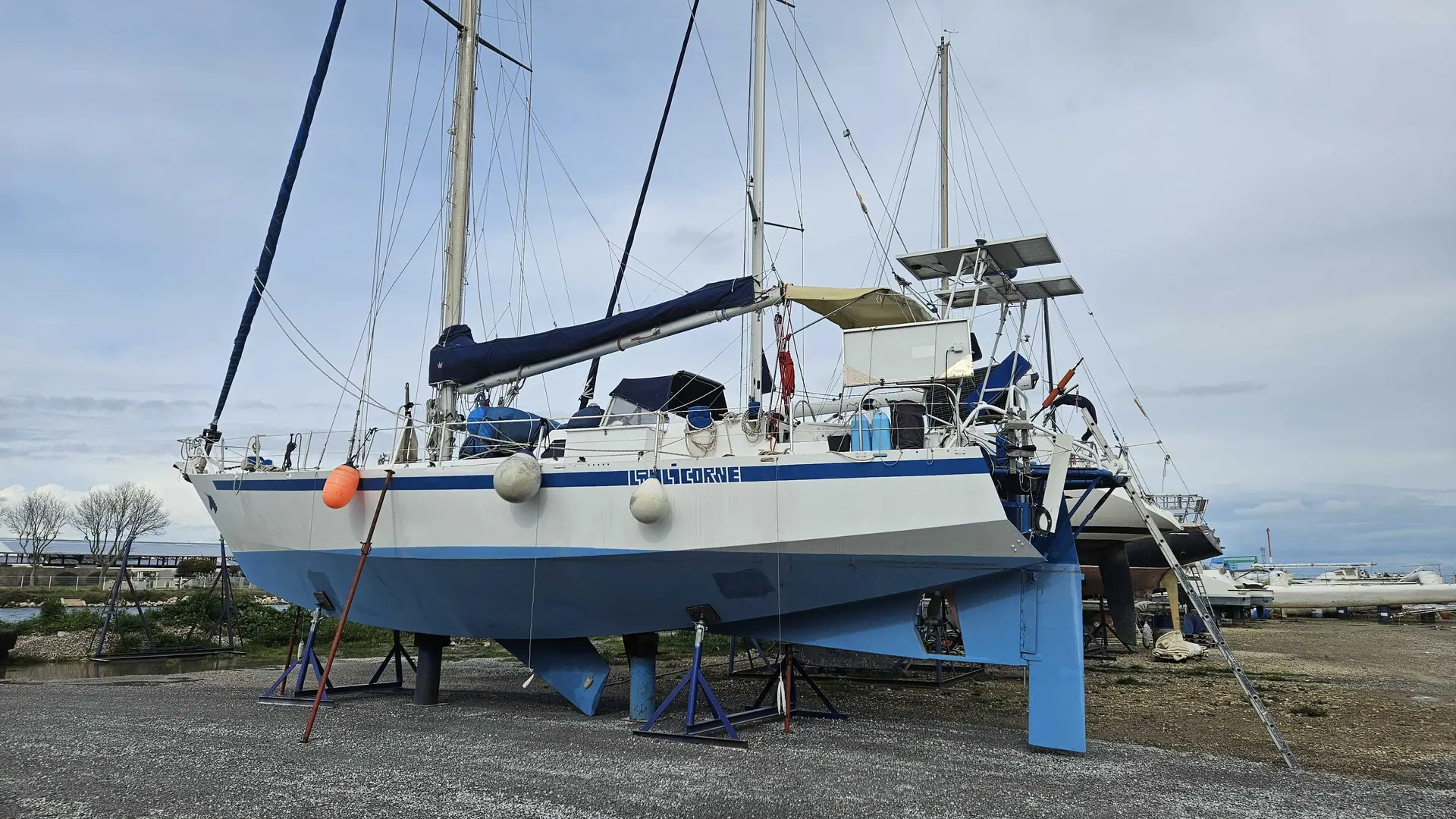 Meta Dalu 47 — Voilier bleu et blanc présenté à terre sur bers dans un chantier maritime.
