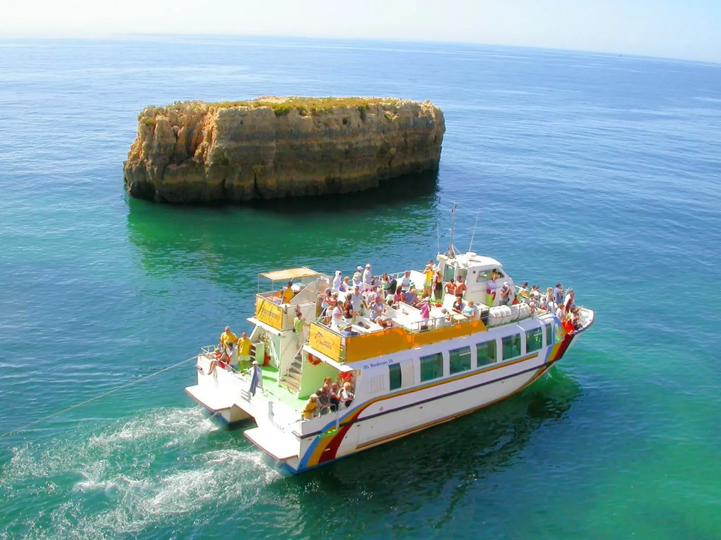 Rodman 59 — Bateau de promenade blanc et orange naviguant près d’un îlot rocheux.