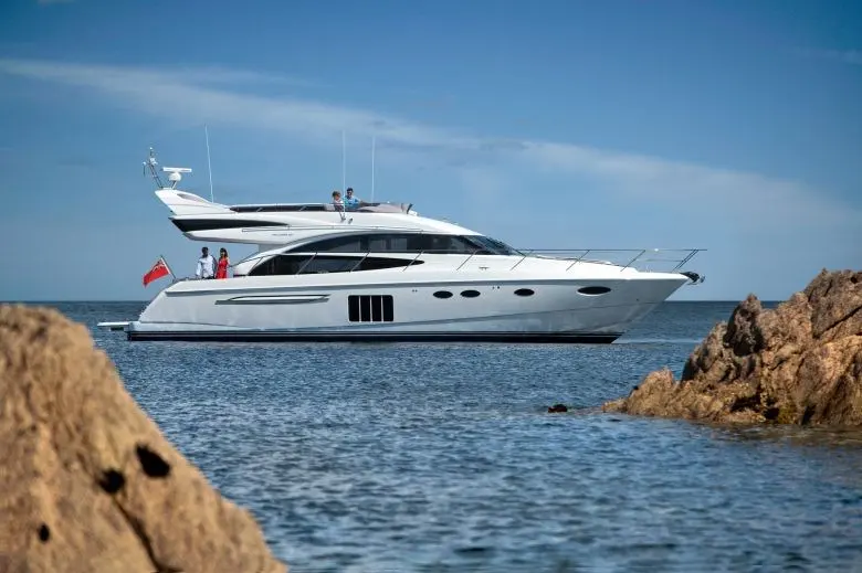 Princess 60 Fly — Yacht à moteur blanc vu de profil entre des rochers, en mer.
