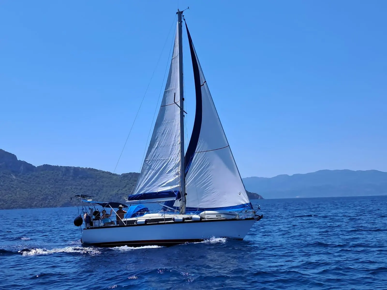 Dufour 3800 — Voilier blanc naviguant sous voiles devant une côte montagneuse.