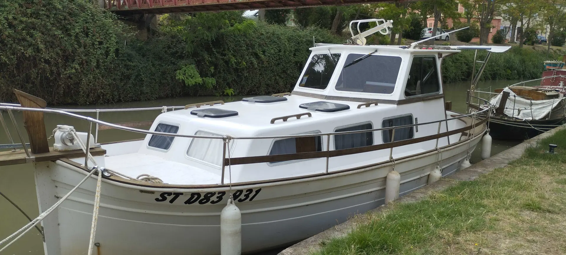 Majoni Espalmador — Bateau à cabine blanc amarré sur un canal, vu de trois quarts avant.