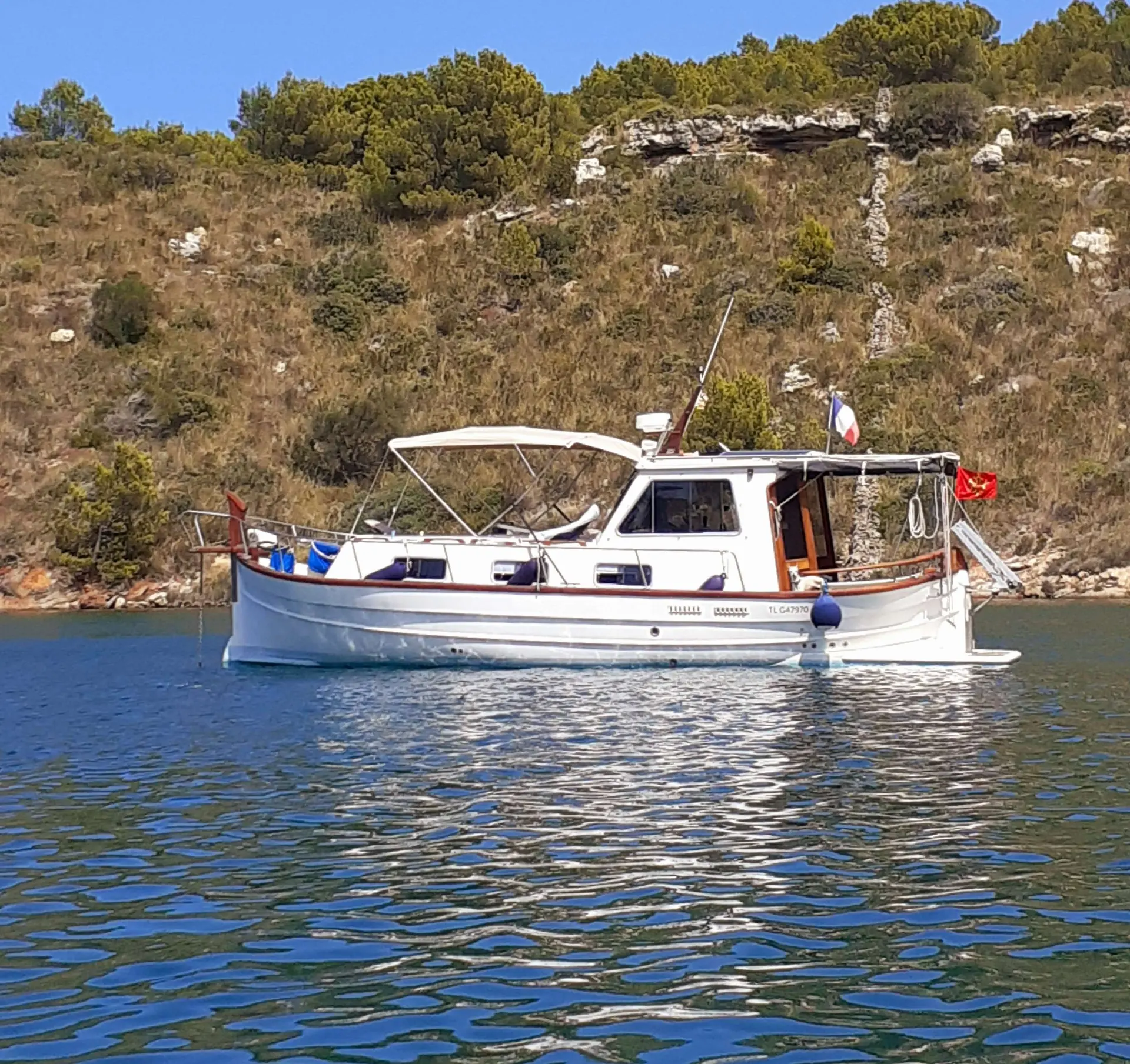 Menorquin 55 — Bateau à moteur vu de profil, amarré devant une côte rocheuse.