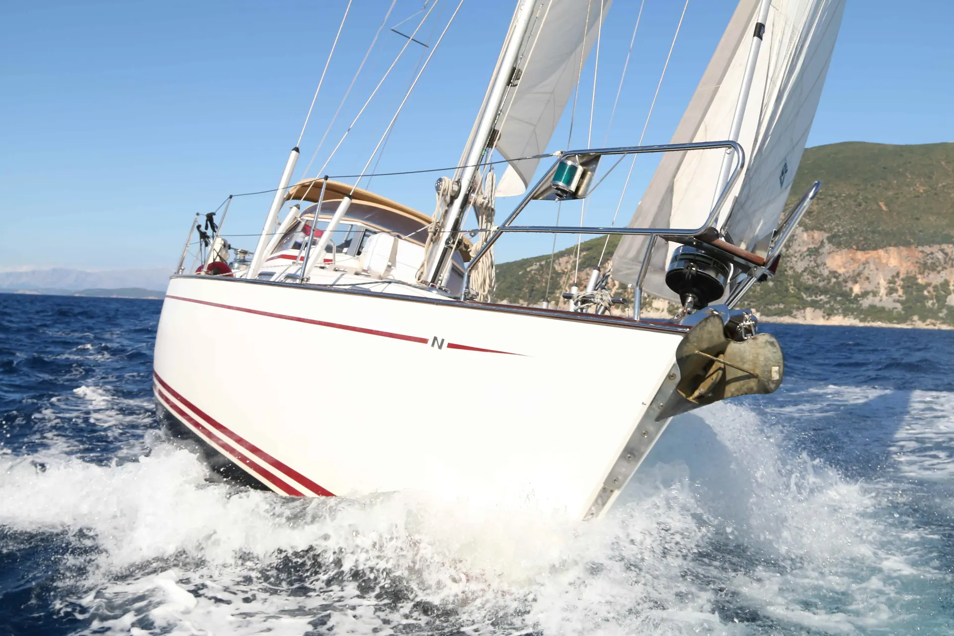 Najad 380 — Voilier blanc vu de trois quarts avant, naviguant au large d’une côte rocheuse.