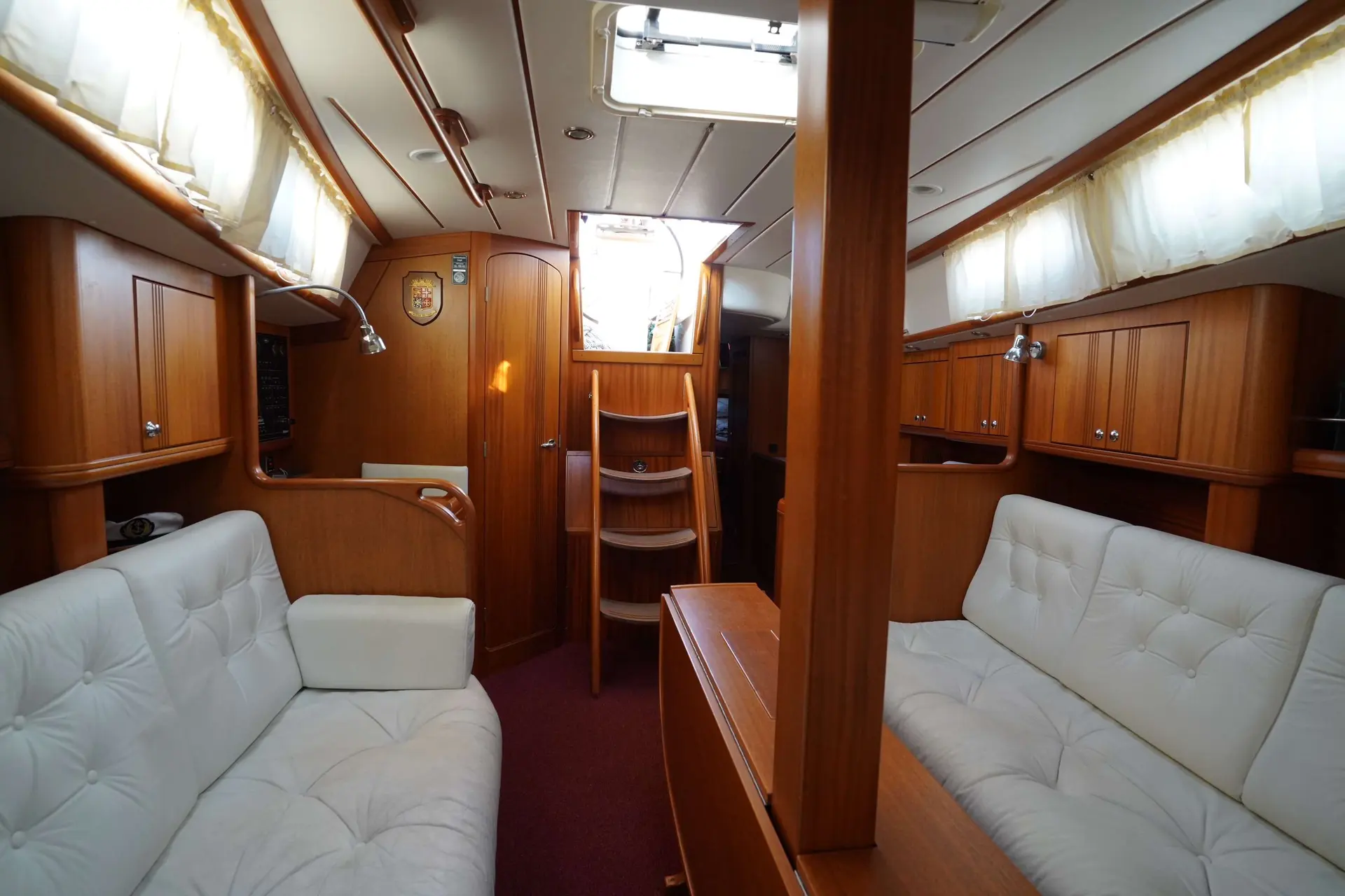 Najad 380 — Salon intérieur en bois avec banquettes, rangements et descente centrale.