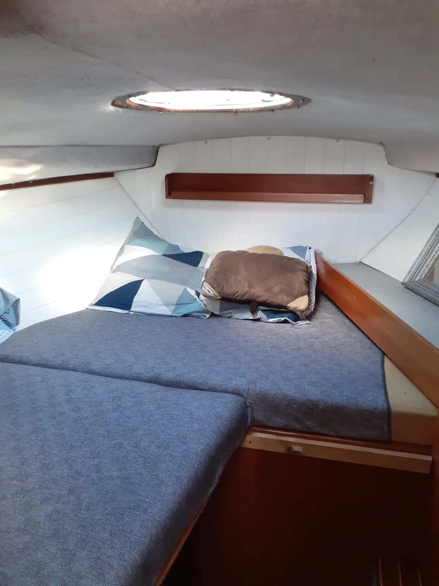 Ocqueteau 760 — Couchette avant avec literie, hublot de pont et rangement mural en bois.