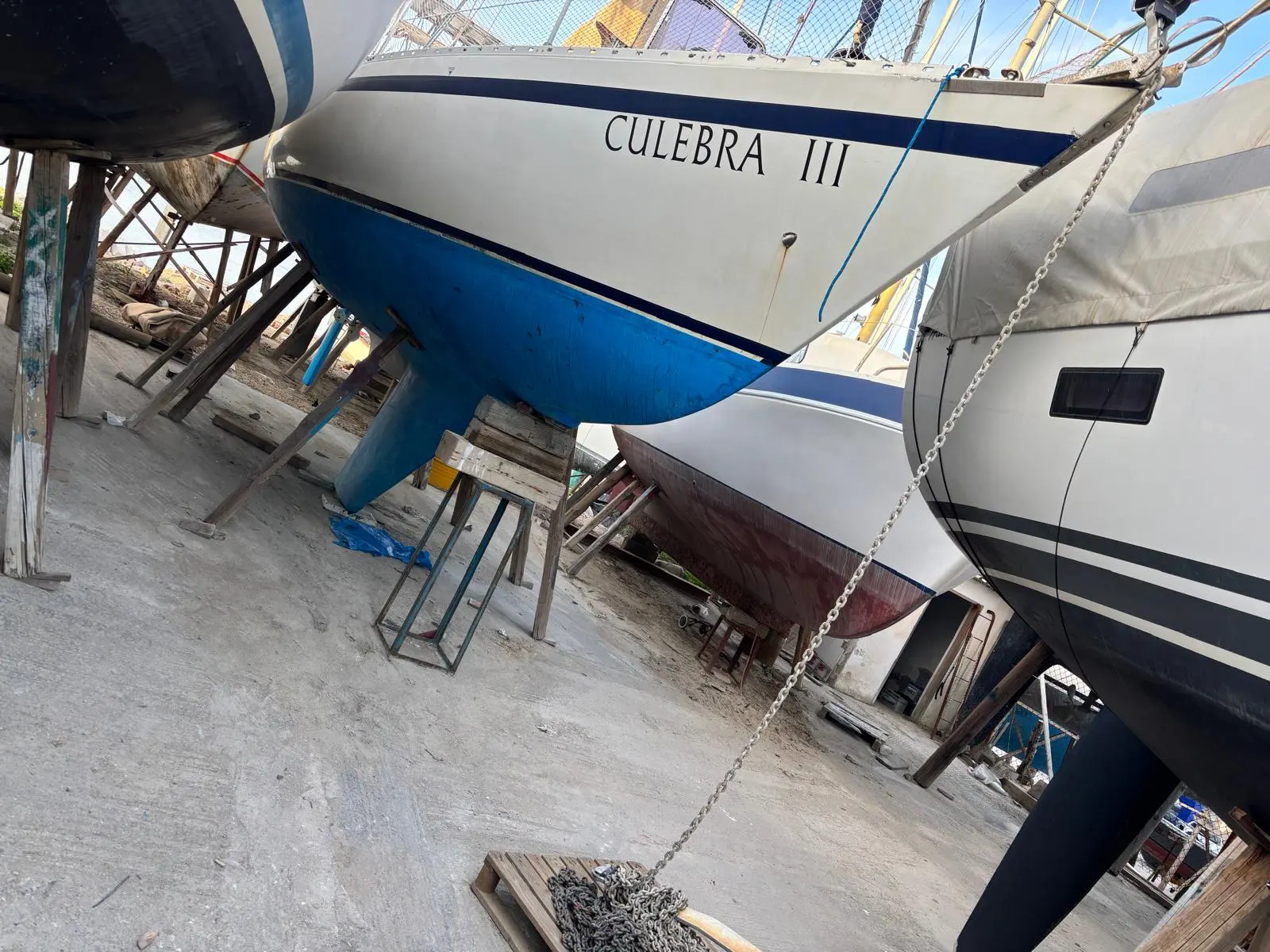UFO 34 — Voilier à coque bleue photographié à terre parmi d’autres bateaux.