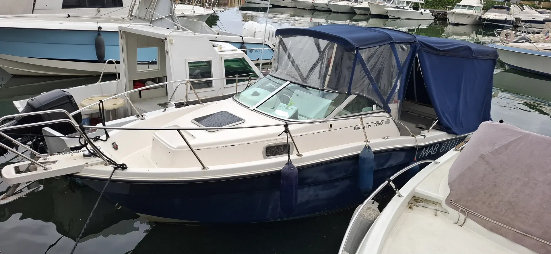 Karnic Bluewater 2260 — Bateau à moteur blanc et bleu amarré dans un port, vu de trois quarts.