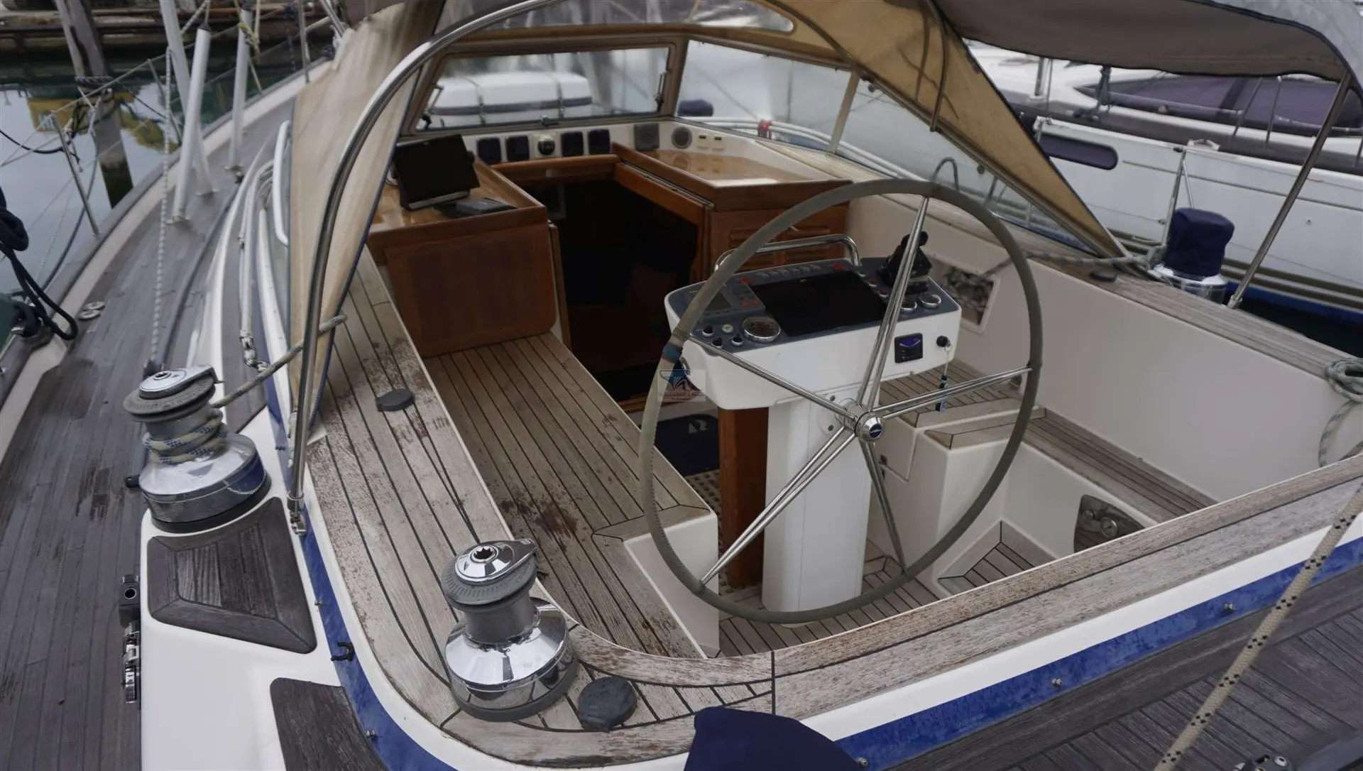 Hallberg Rassy 48 — Vue du cockpit et de la descente d’un voilier amarré, avec sa barre et ses winchs.