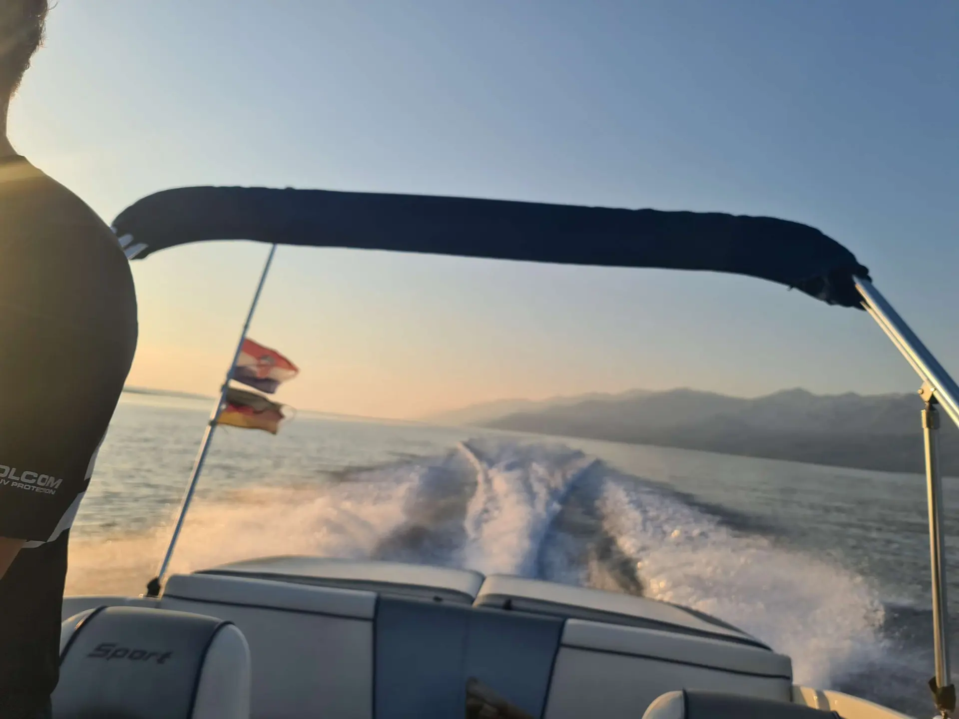 Sea Ray 185 Sport — Vue arrière d’un bateau en navigation, avec sillage, sièges et paysage côtier.