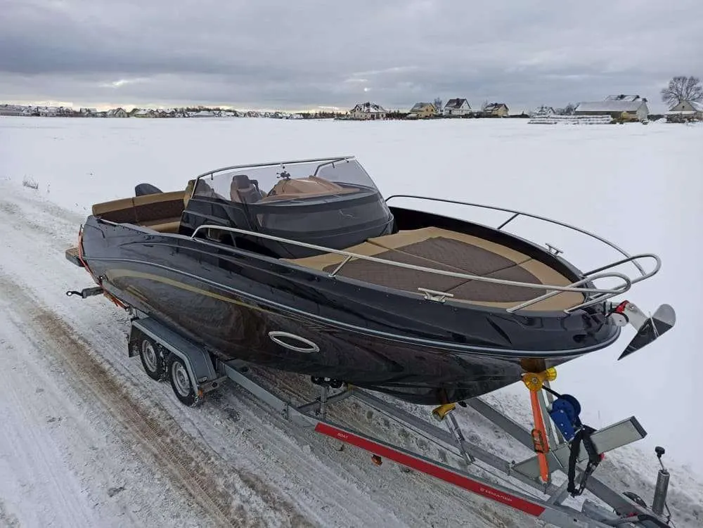 Marine Time QX 620 — Bateau à moteur noir sur remorque, photographié dans un paysage enneigé.
