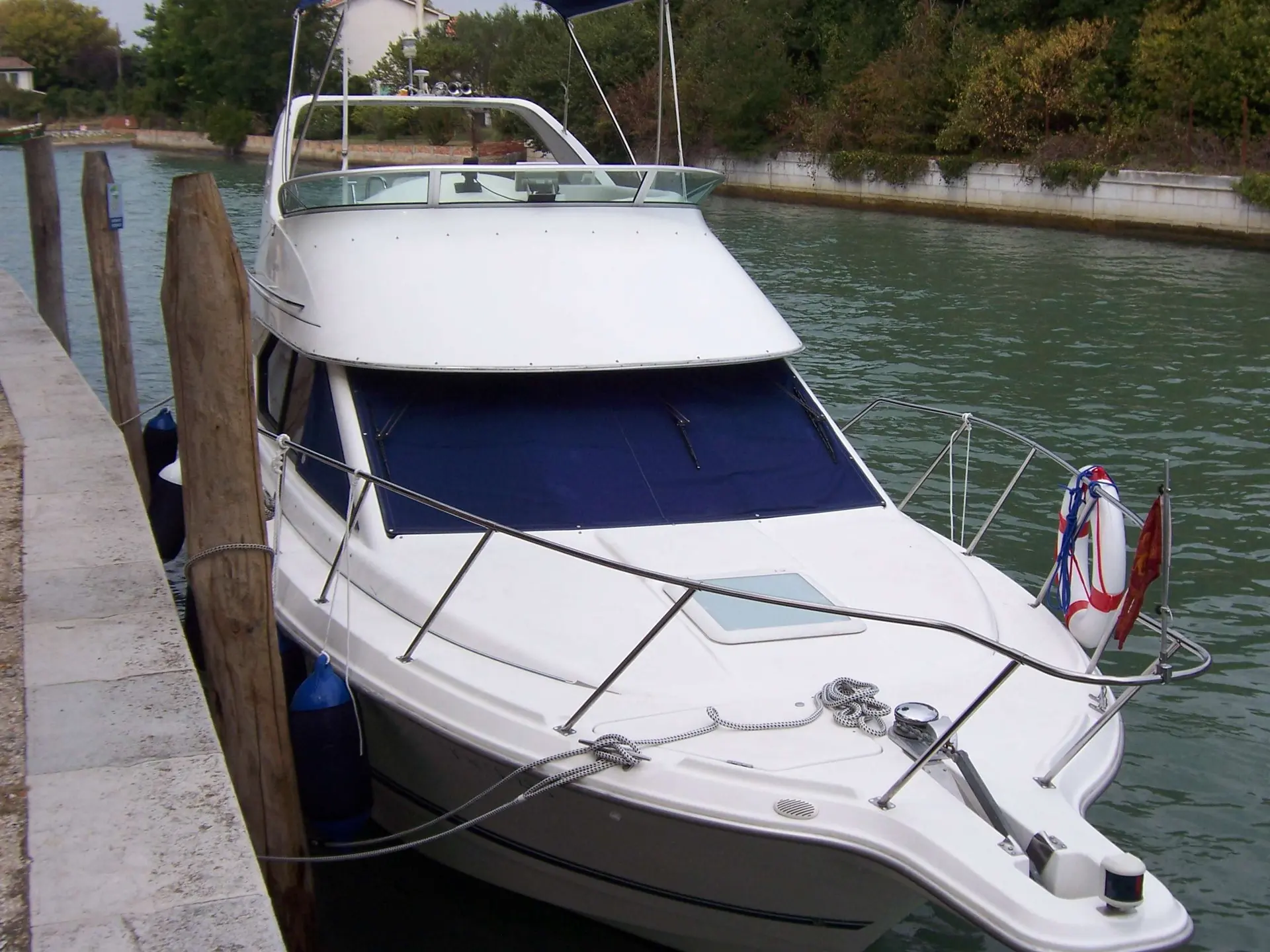 Bayliner 2858 Fly — Bateau à moteur blanc amarré dans un canal, vu de trois quarts avant.