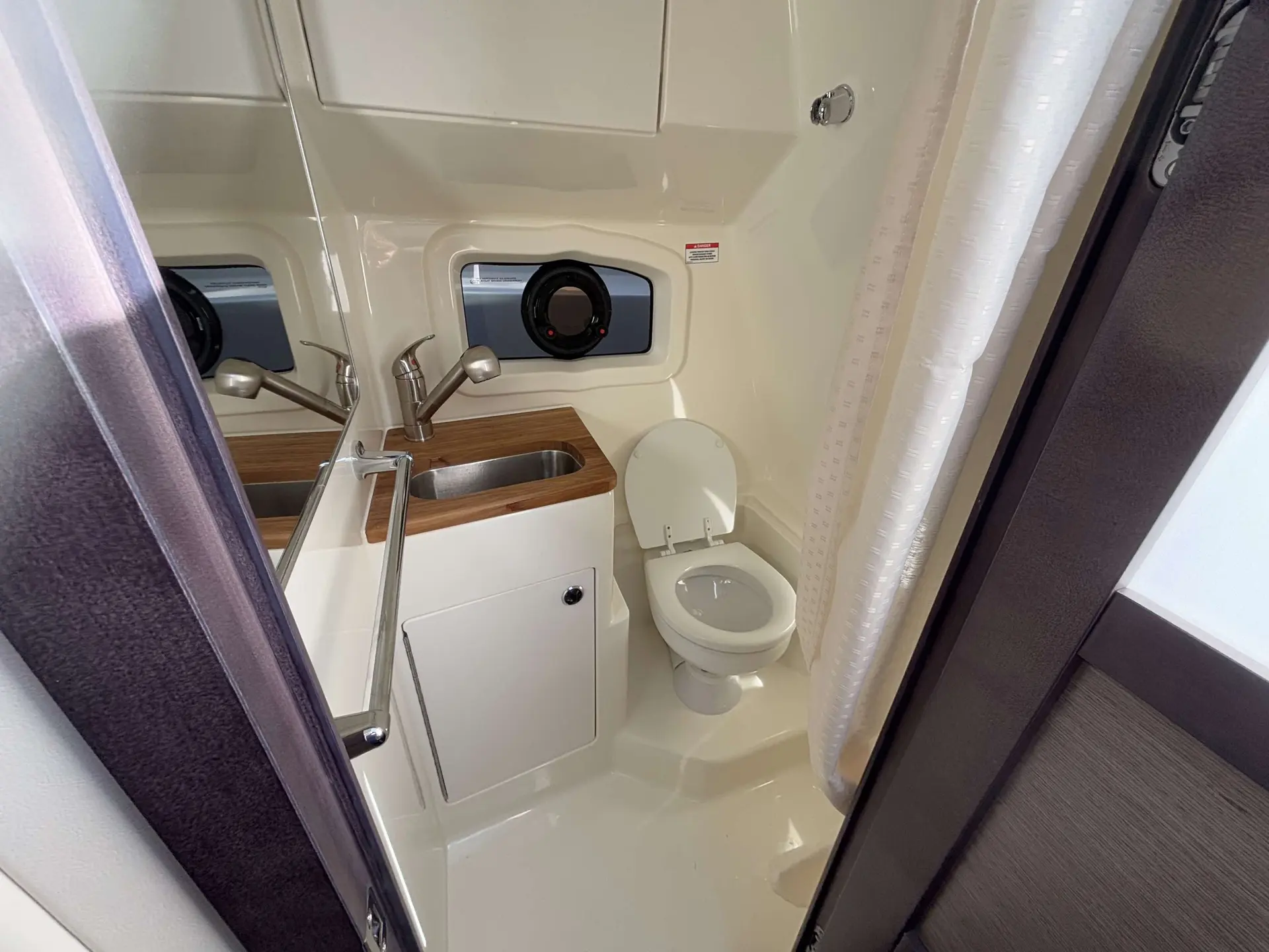 Bayliner Ciera 8 — Salle d’eau avec lavabo, miroir, hublot et toilettes à bord du bateau.