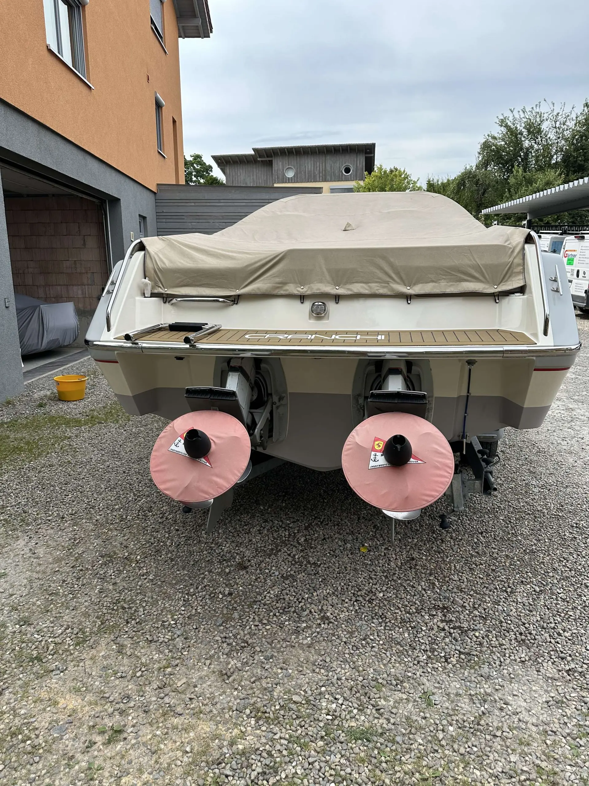 Cranchi Clipper 760 — Vue arrière d’un bateau à moteur bâché, stationné sur une aire gravillonnée.