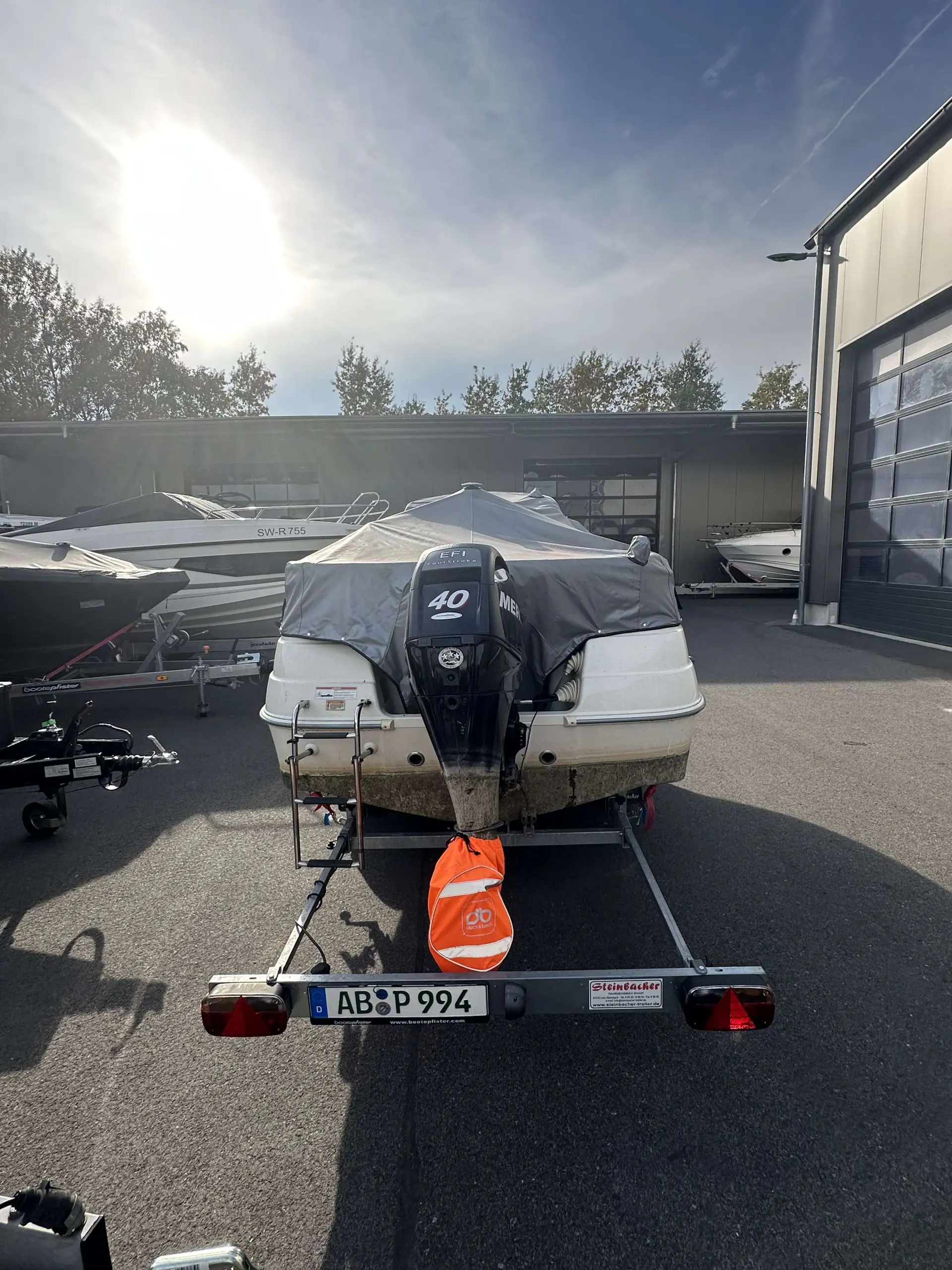 Quicksilver Activ 430 Cabin — Bateau à moteur bâché vu de l’arrière, stationné sur une remorque devant un bâtiment.