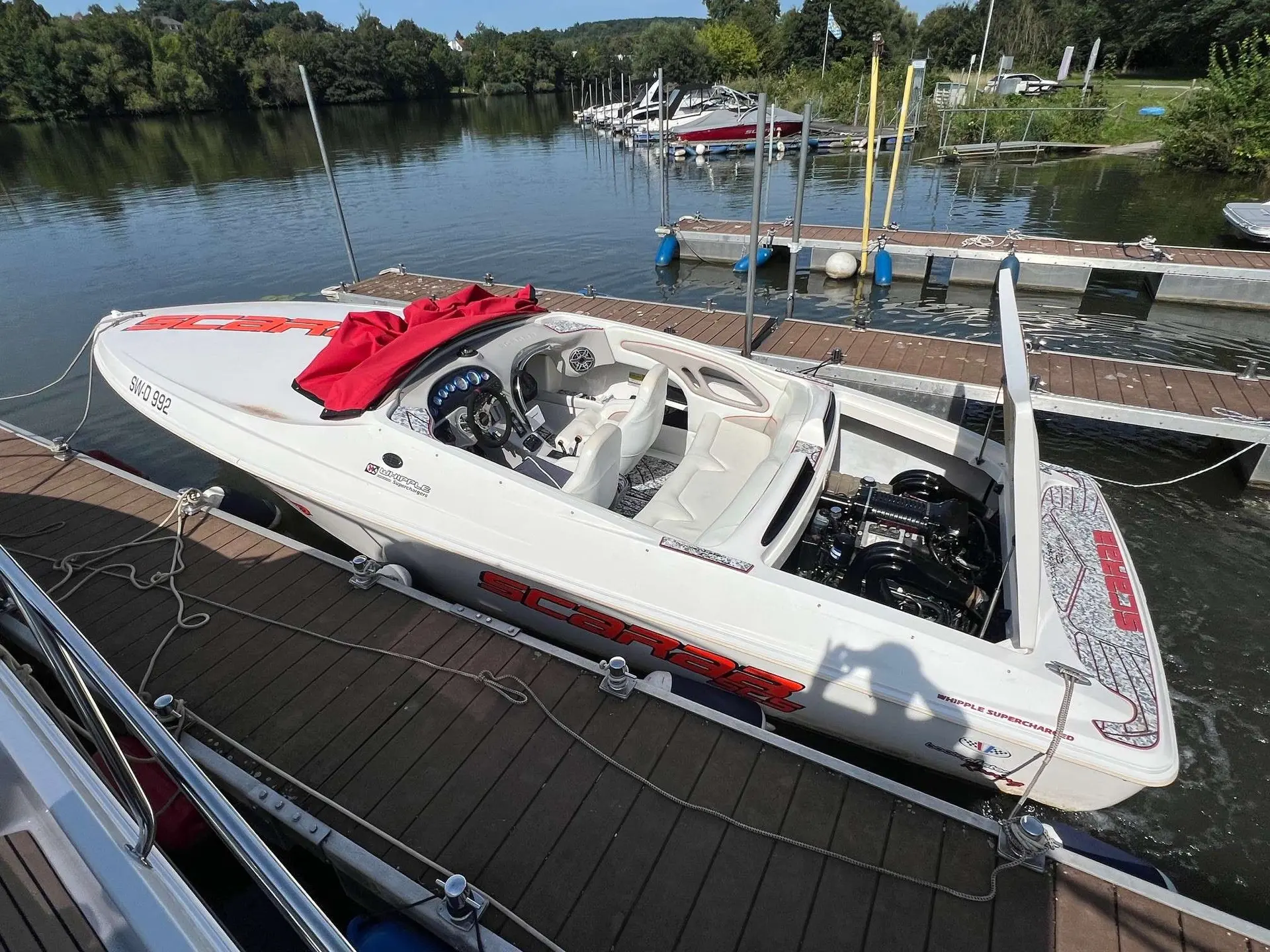 Scarab Boats Scarab — Bateau à moteur blanc amarré à un ponton, vu de trois quarts avec cockpit ouvert.