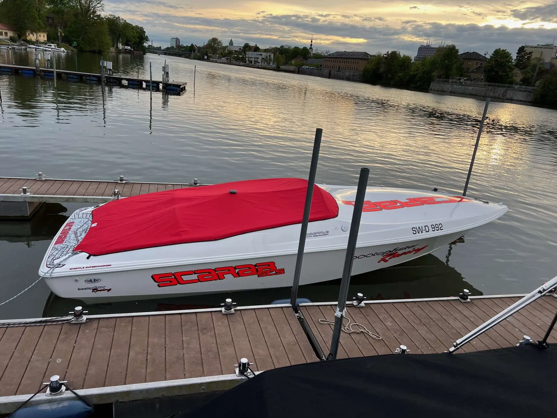 Scarab Boats Scarab — Bateau Scarab blanc et rouge amarré sur un ponton, vu de profil.