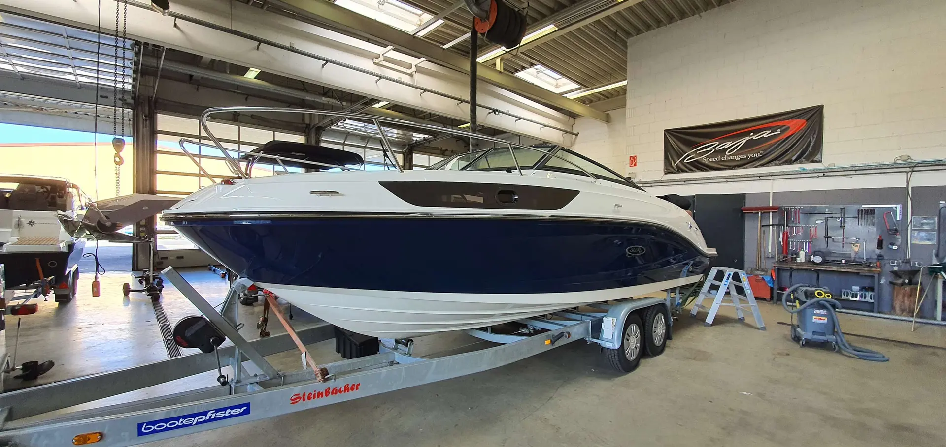 Sea Ray 230 SSE — Bateau à moteur blanc et bleu sur remorque, photographié dans un atelier.